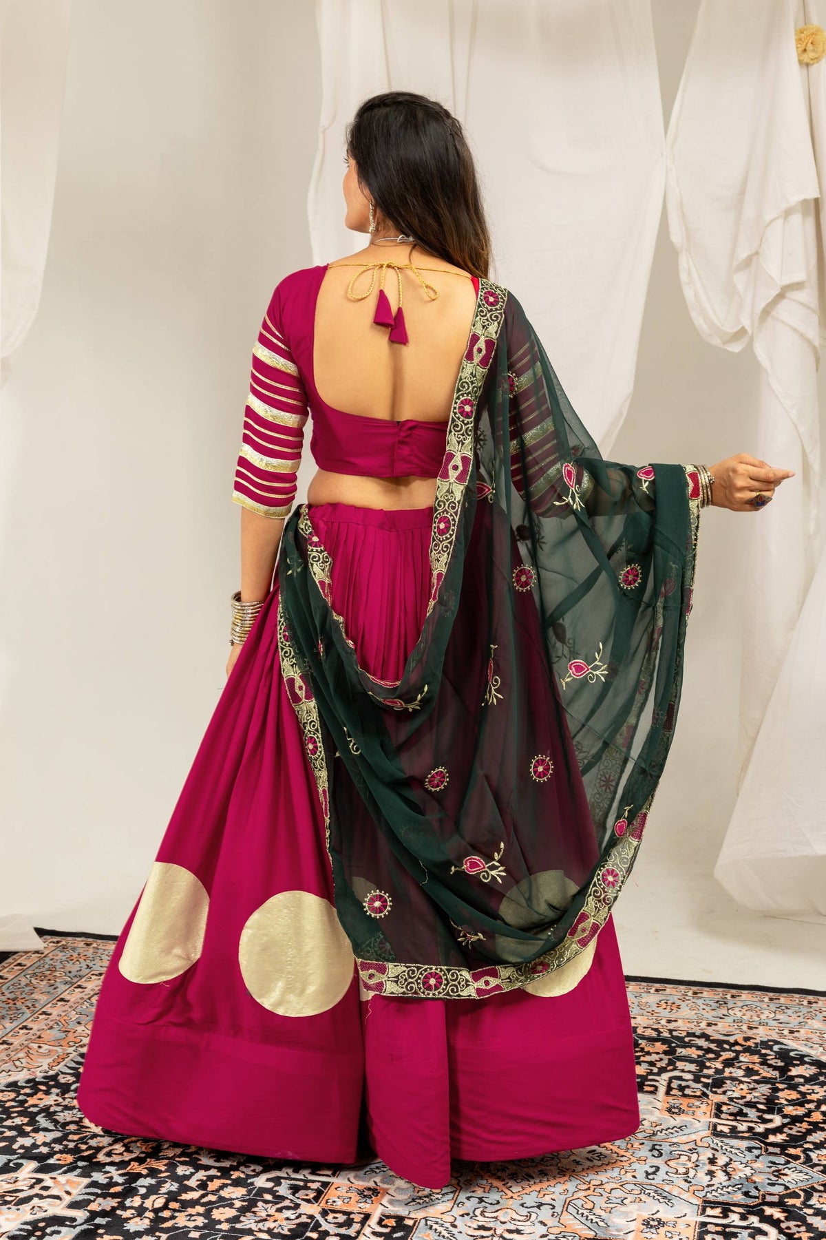 Back view of a model showing the deep square back neckline with tie-up tassels on a magenta choli and matching skirt.