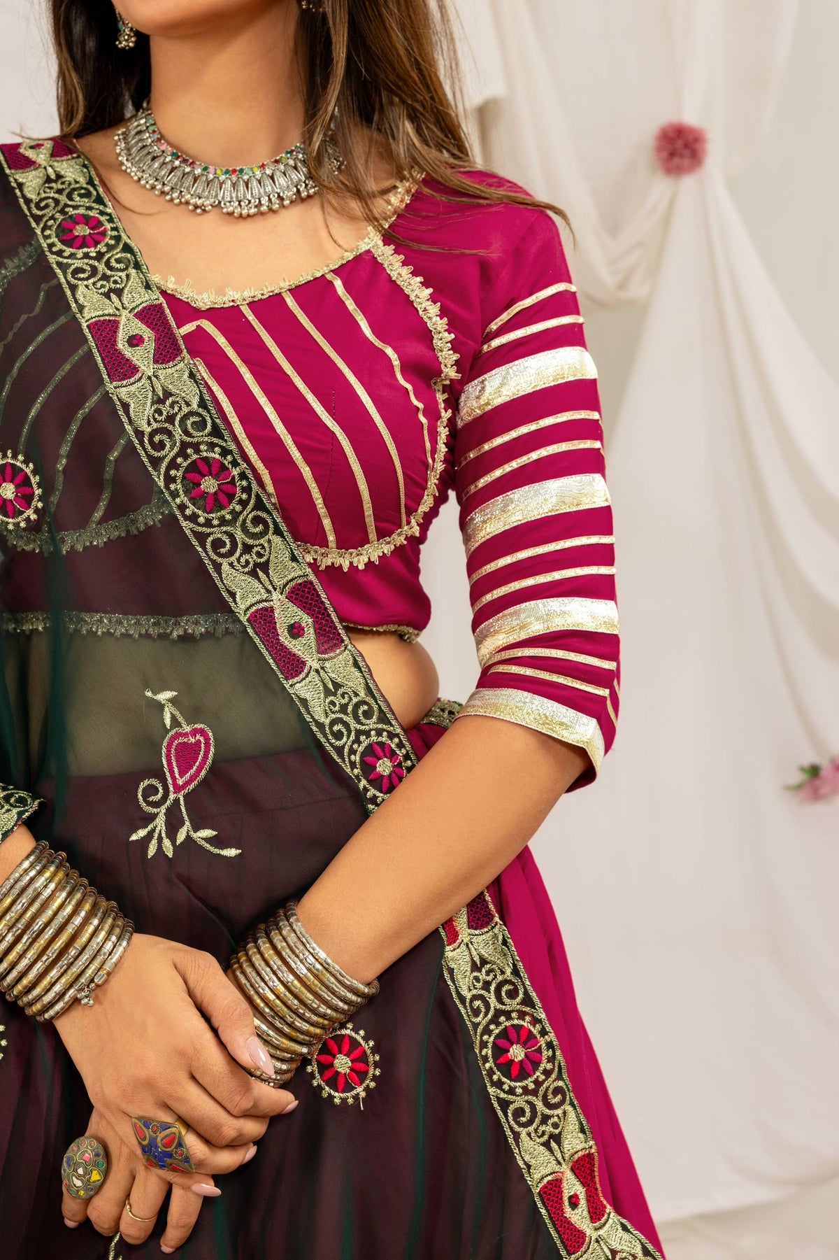 Close-up view of a magenta choli featuring gold linear striped embroidery, lace trims, and a dark green border dupatta.