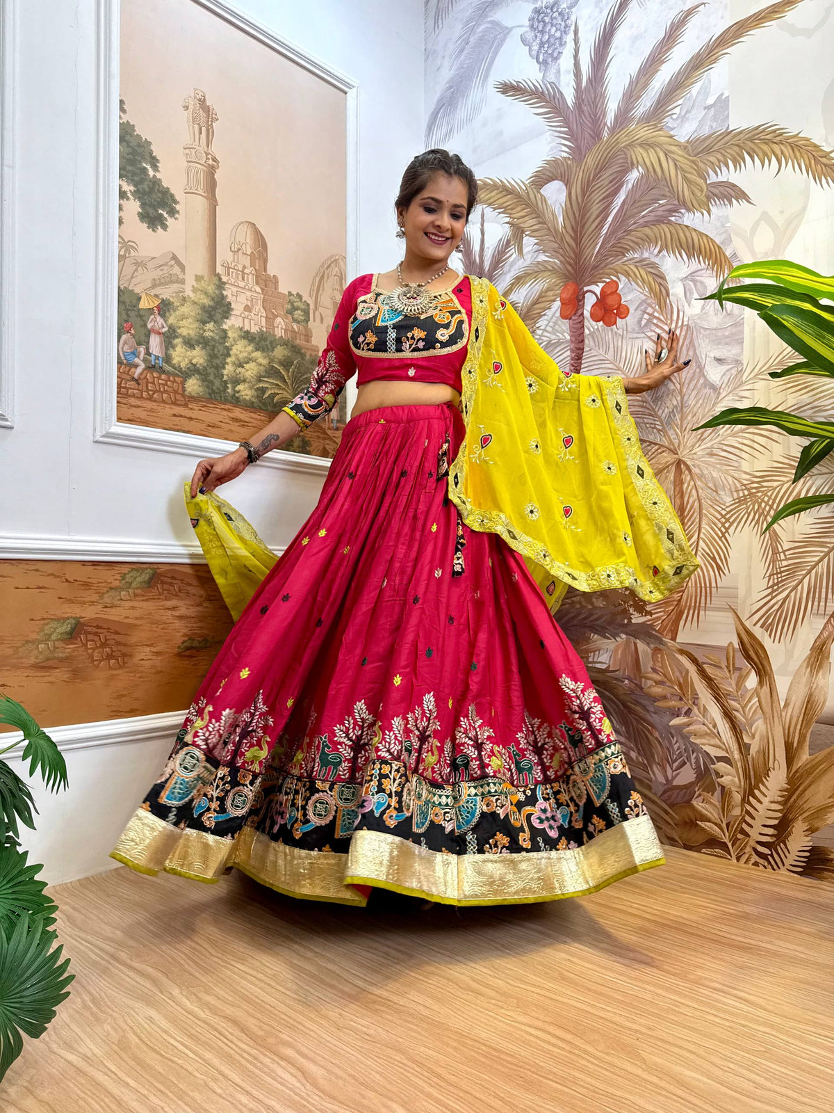 Model wearing a magenta pink flared lehenga and black embroidered yoke blouse with an open yellow dupatta drape