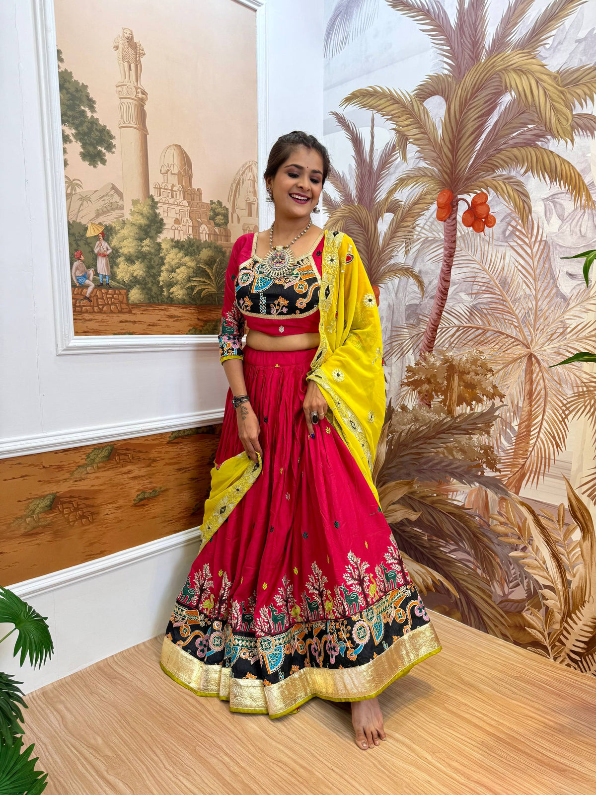 Full-length front shot of model in a gathered magenta pink lehenga skirt with multi-color printed hem and yellow dupatta