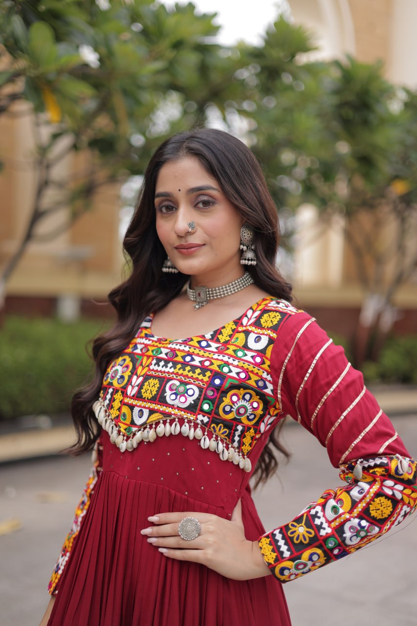 Close-up portrait highlighting the multi-color Gamthi embroidered yoke, cowrie shell drops, and tribal choker on a maroon gown