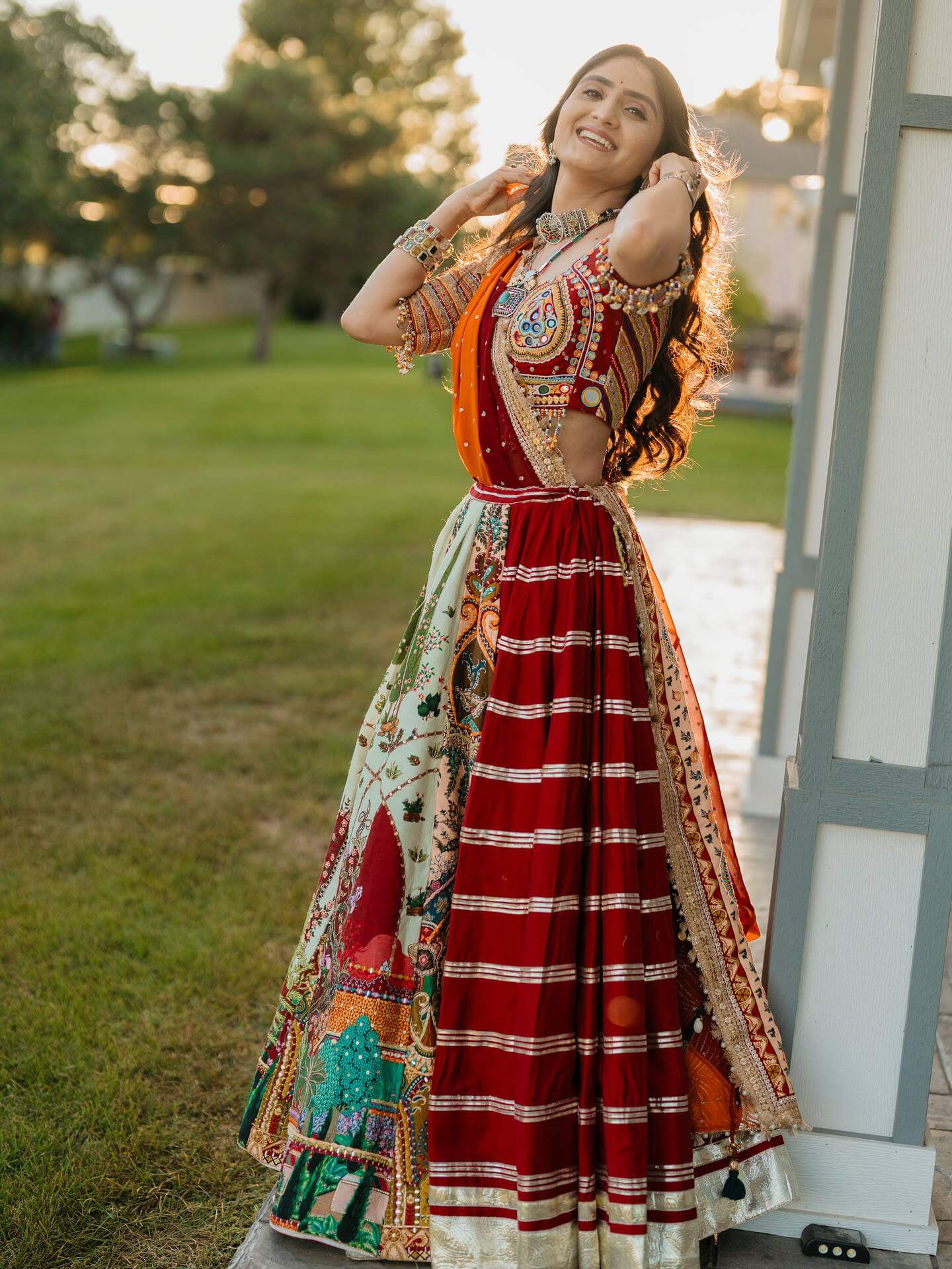 Side view of model in panelled lehenga with red striped gota patti section, pictorial print kali, and embroidered blouse