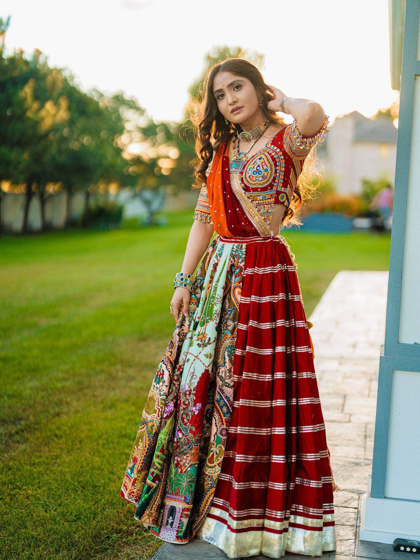 Front-angle full view of model in a red panelled lehenga with metallic hem border, multicolor print panels, and mirror choli