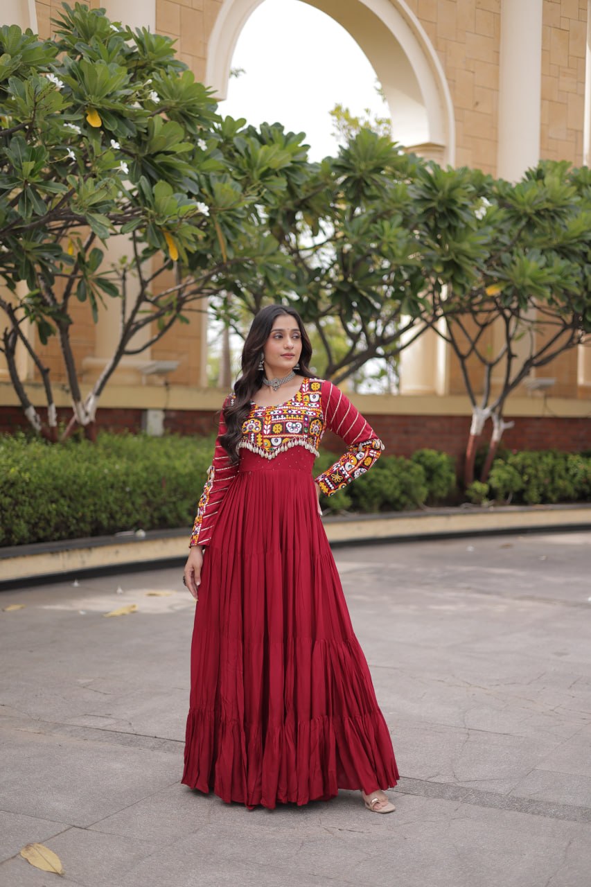 Standing full-length front view of a model in a maroon tiered full-sleeve anarkali gown with cowrie shell fringe hemline