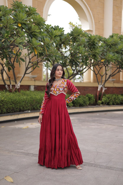 Standing full-length front view of a model in a maroon tiered full-sleeve anarkali gown with cowrie shell fringe hemline