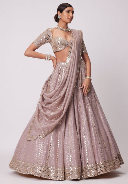 Side-angle full-length shot of a model wearing a mauve-pink mirror-embellished flared lehenga with cowled front dupatta drape