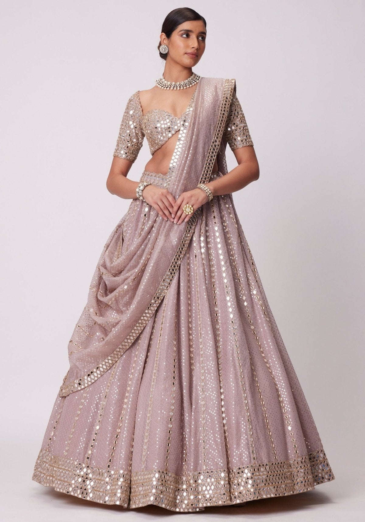 Standing full-length front view of a model in a mauve-pink flared lehenga with vertical mirror lines, matching dupatta drape, and embroidered blouse