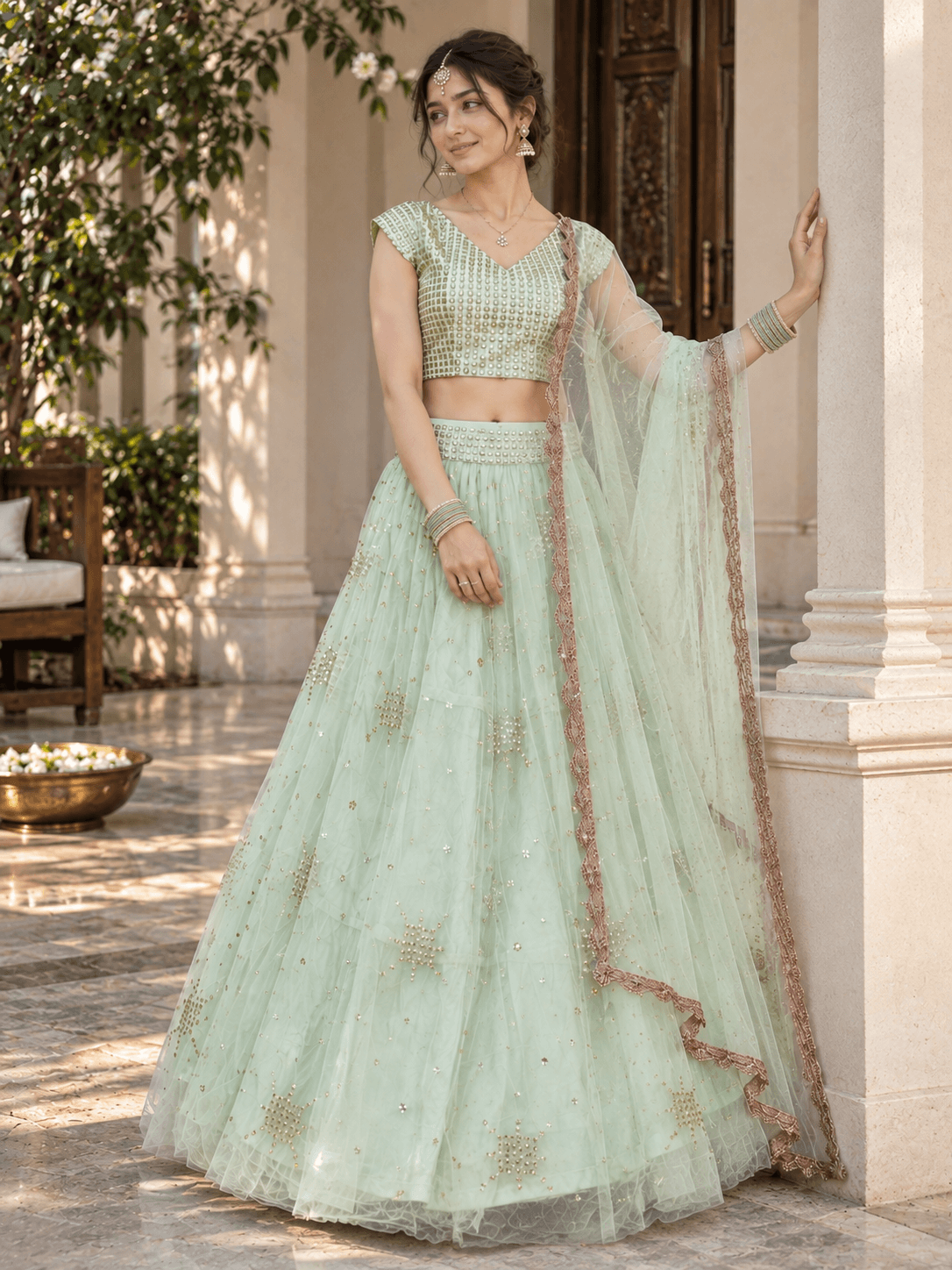 Model leaning against a pillar wearing a mint green sequin-embroidered lehenga with scalloped net dupatta