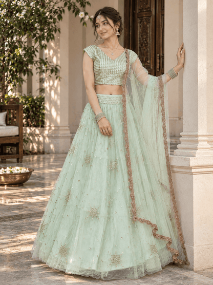 Model leaning against a pillar wearing a mint green sequin-embroidered lehenga with scalloped net dupatta