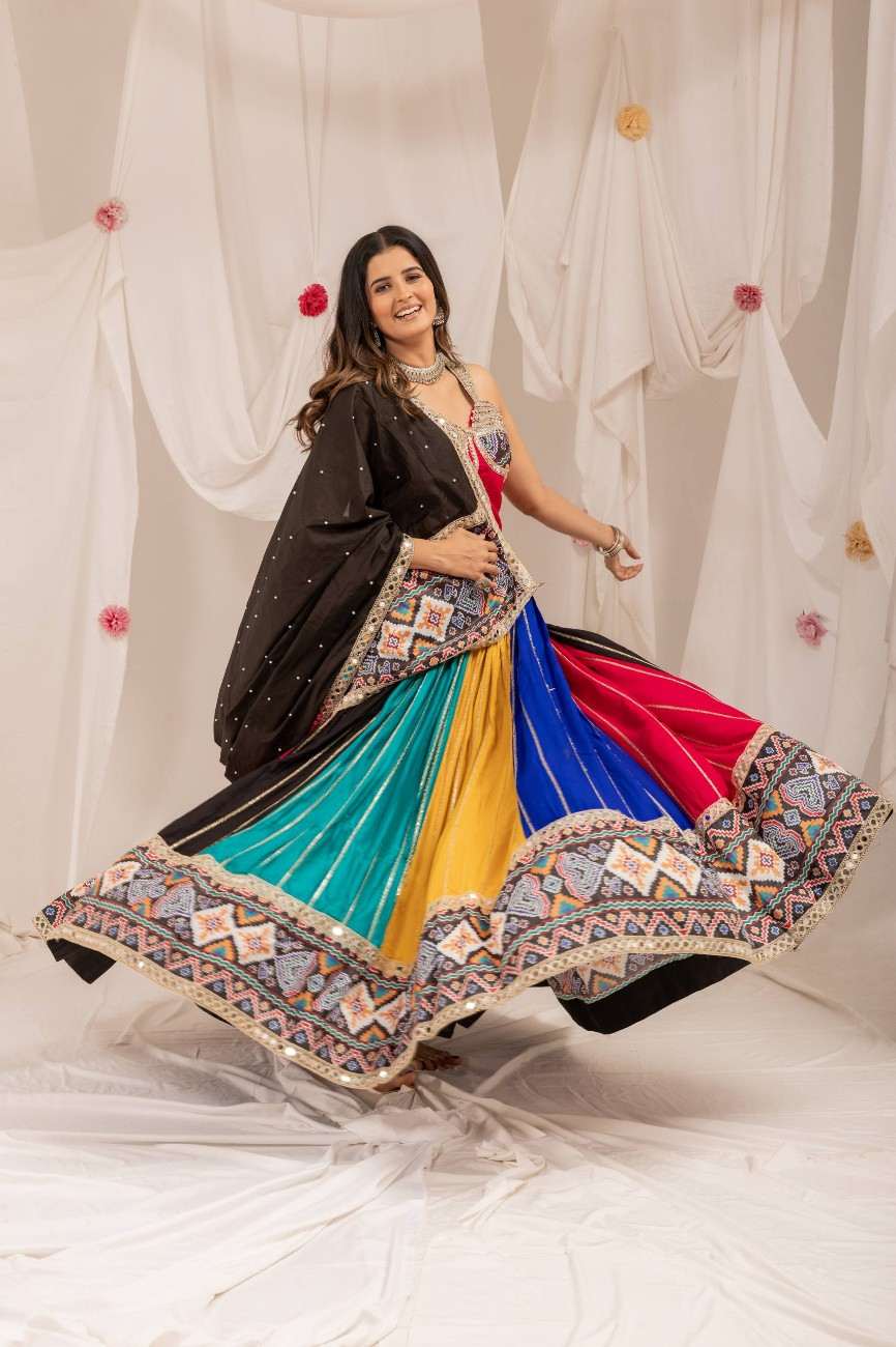 Model twirling in a multicolor pleated lehenga skirt displaying a wide flare and ornate geometric border.