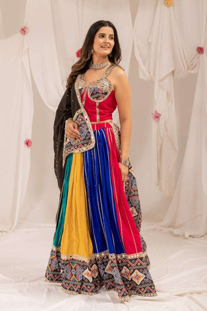 Standing three-quarter pose of a model dressed in a vibrant multicolor panel lehenga and black dupatta.