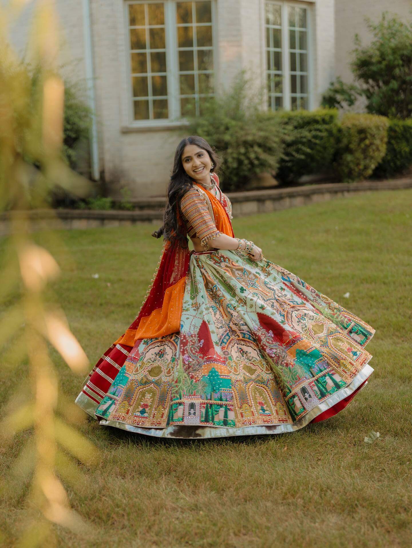 Model twirling outdoors showing the full circumference of a multicolor pictorial print panelled lehenga skirt