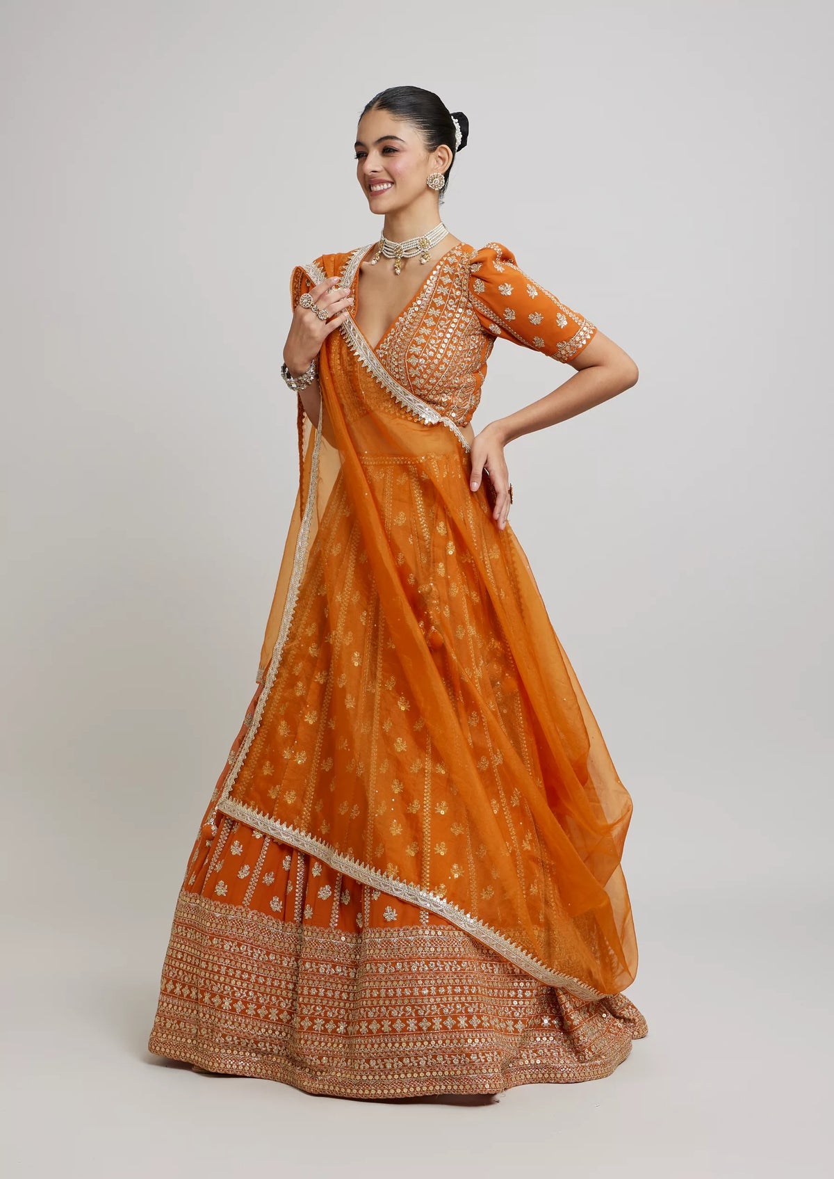 Standing side-angle view showing the wide flare and intricate sequin border of a mustard-orange lehenga with puff-sleeve choli.