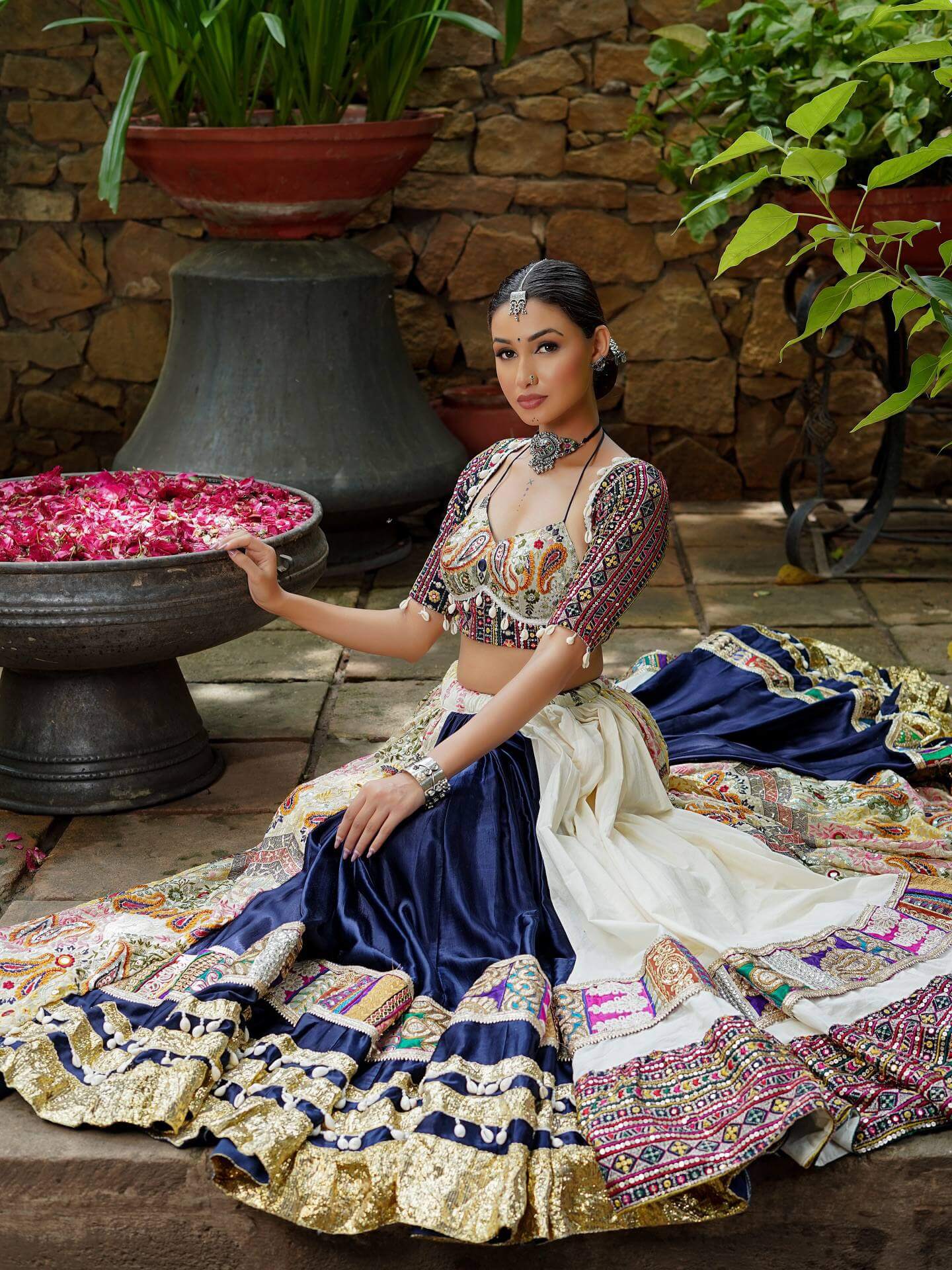 Model seated displaying wide flare off-white and navy blue panelled lehenga with patch border and cowrie lace