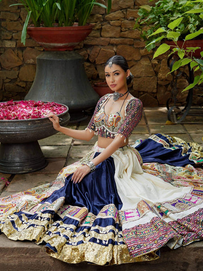 Model seated displaying wide flare off-white and navy blue panelled lehenga with patch border and cowrie lace