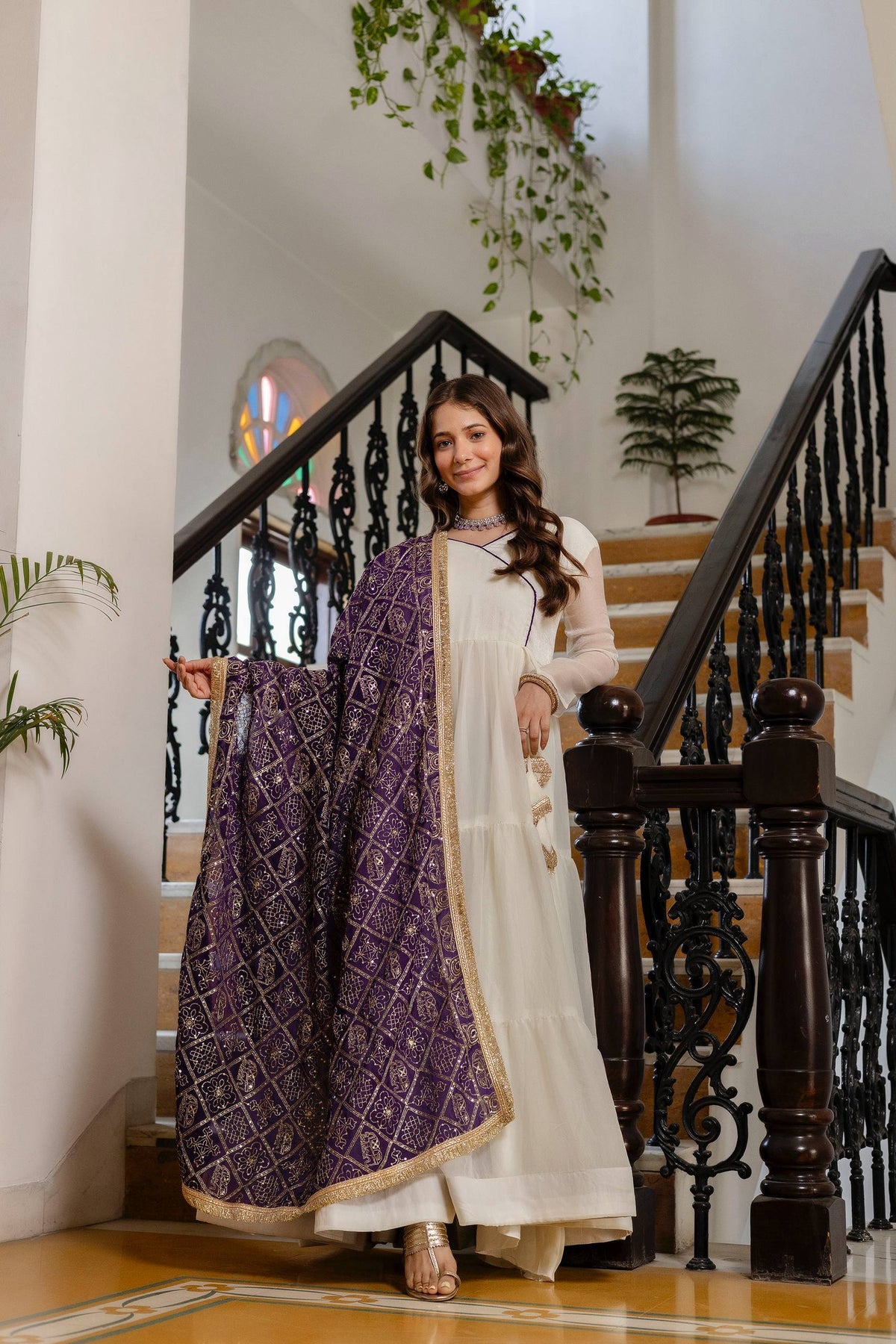 Model in an off-white tiered anarkali suit displaying the full width and patterned border of a deep purple dupatta