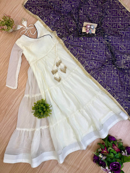Flat lay view of an off-white tiered flare angrakha anarkali suit paired with a deep purple printed dupatta with gold border