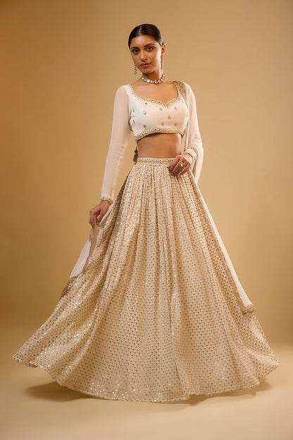 Standing side-angle full-length view showing the flare of an off-white lehenga adorned with gold sequin buttis and a full-sleeve blouse.