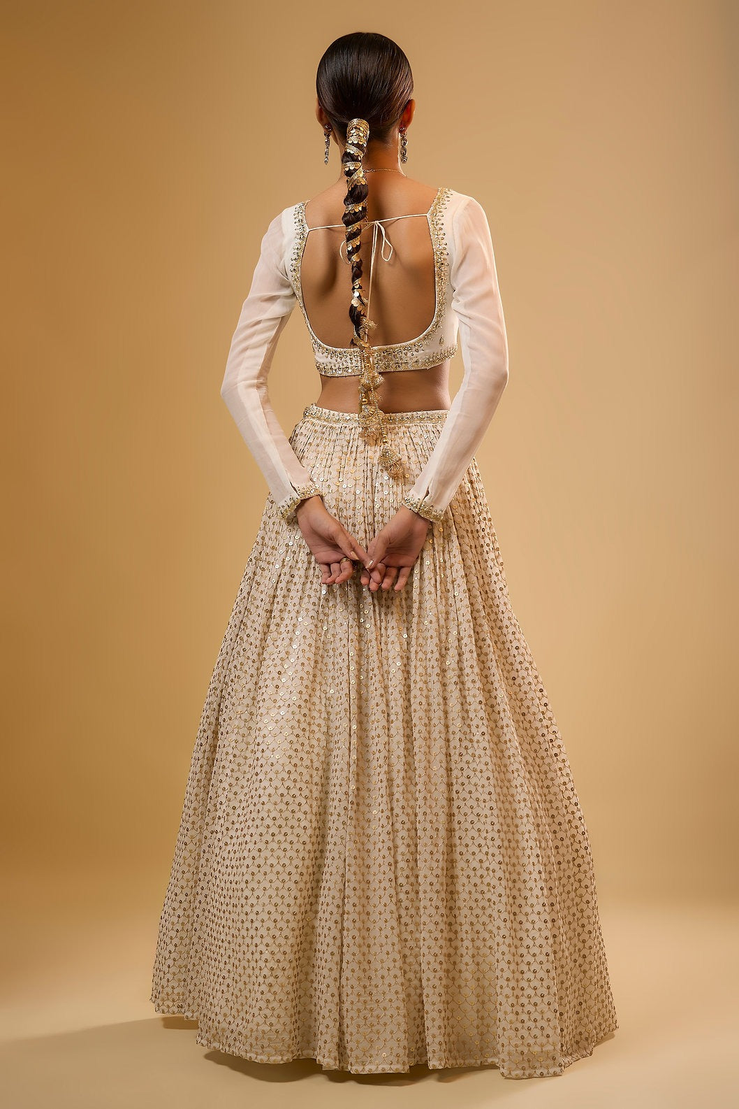 Full-length back view of a model showcasing the low-cut open back blouse with sheer full sleeves and flared off-white embroidered lehenga skirt.