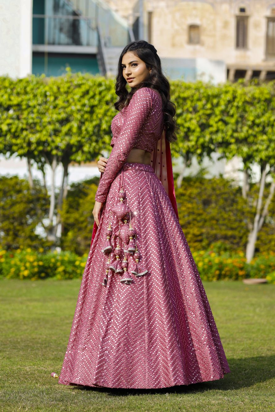 Side profile full-length view showcasing the hanging tiered latkan tassels and allover geometric embroidery of an onion-pink lehenga.