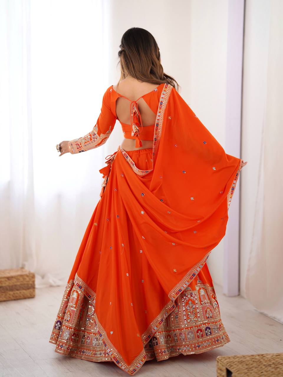 Back view of model wearing an orange lehenga with tie-up back blouse and heavy jharokha embroidered hemline