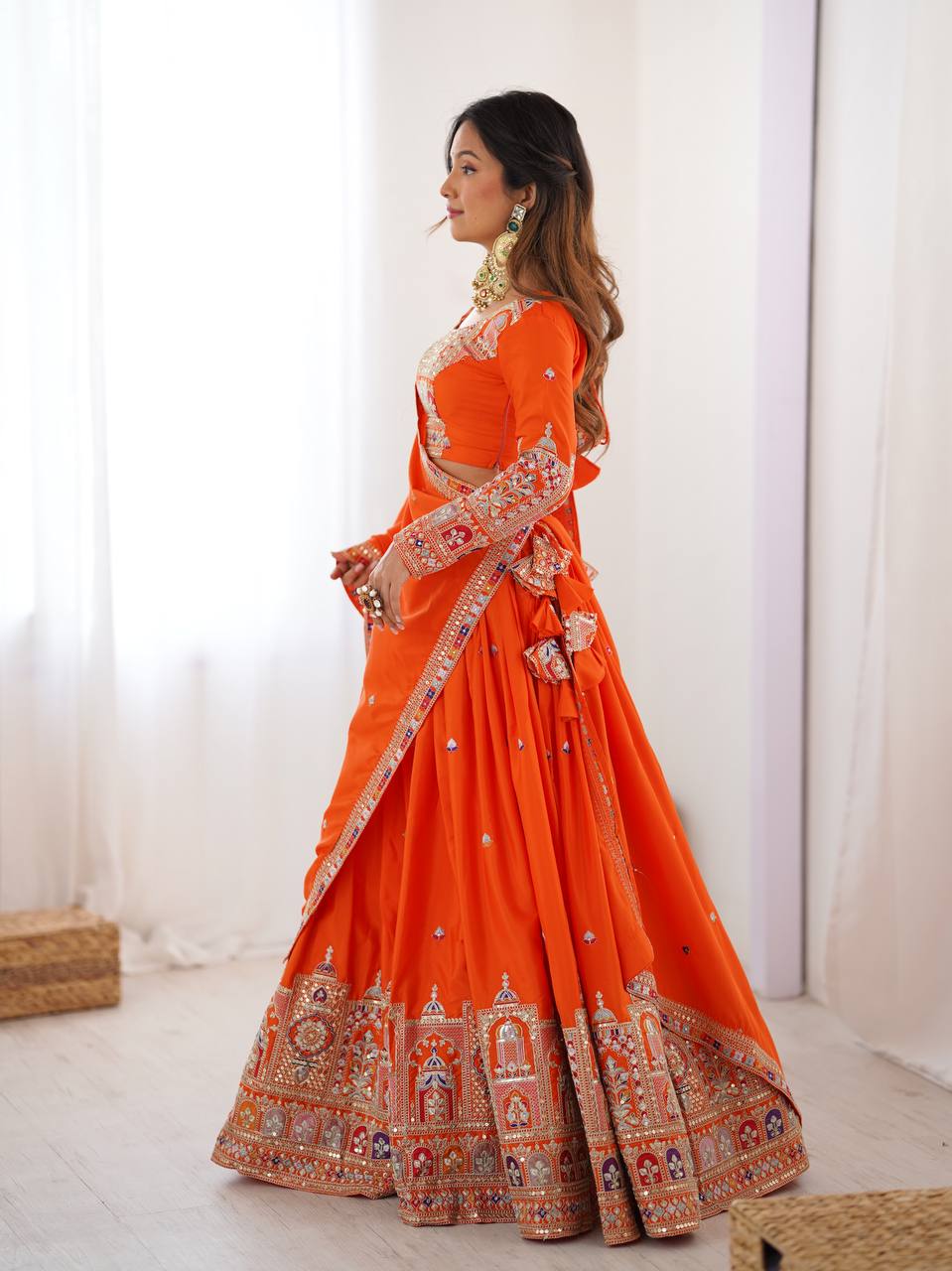 Side view of model wearing an orange pleated lehenga choli with traditional embroidered border and matching dupatta