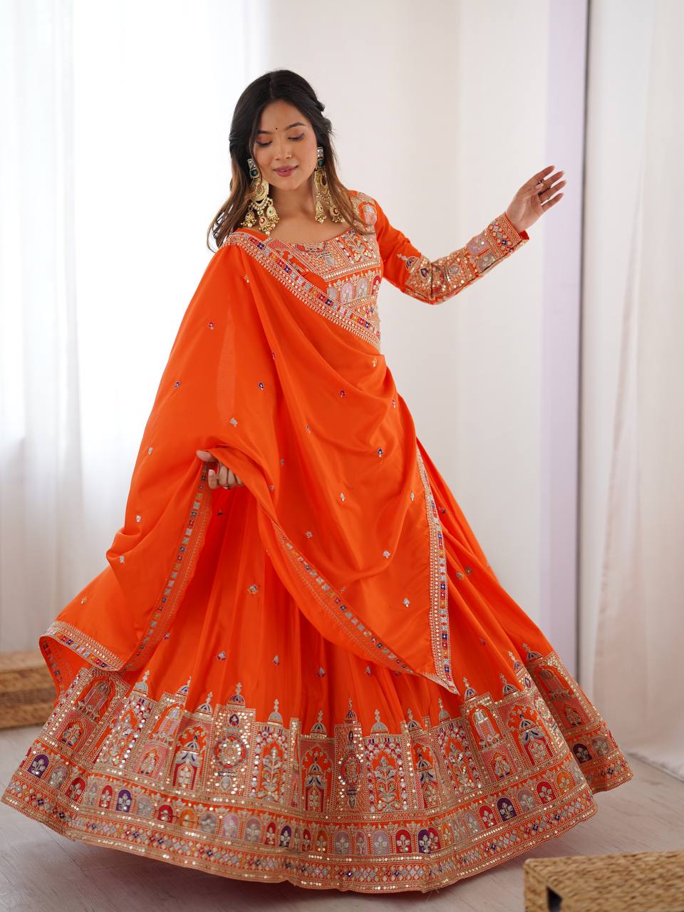 Front angle of model displaying the wide flare and embellished hemline of an orange traditional lehenga