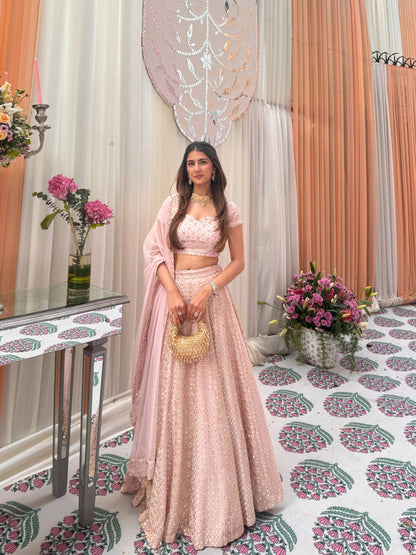 Full-length front view of a model wearing a pastel-pink sequined lehenga choli set styled with a traditional gold choker necklace