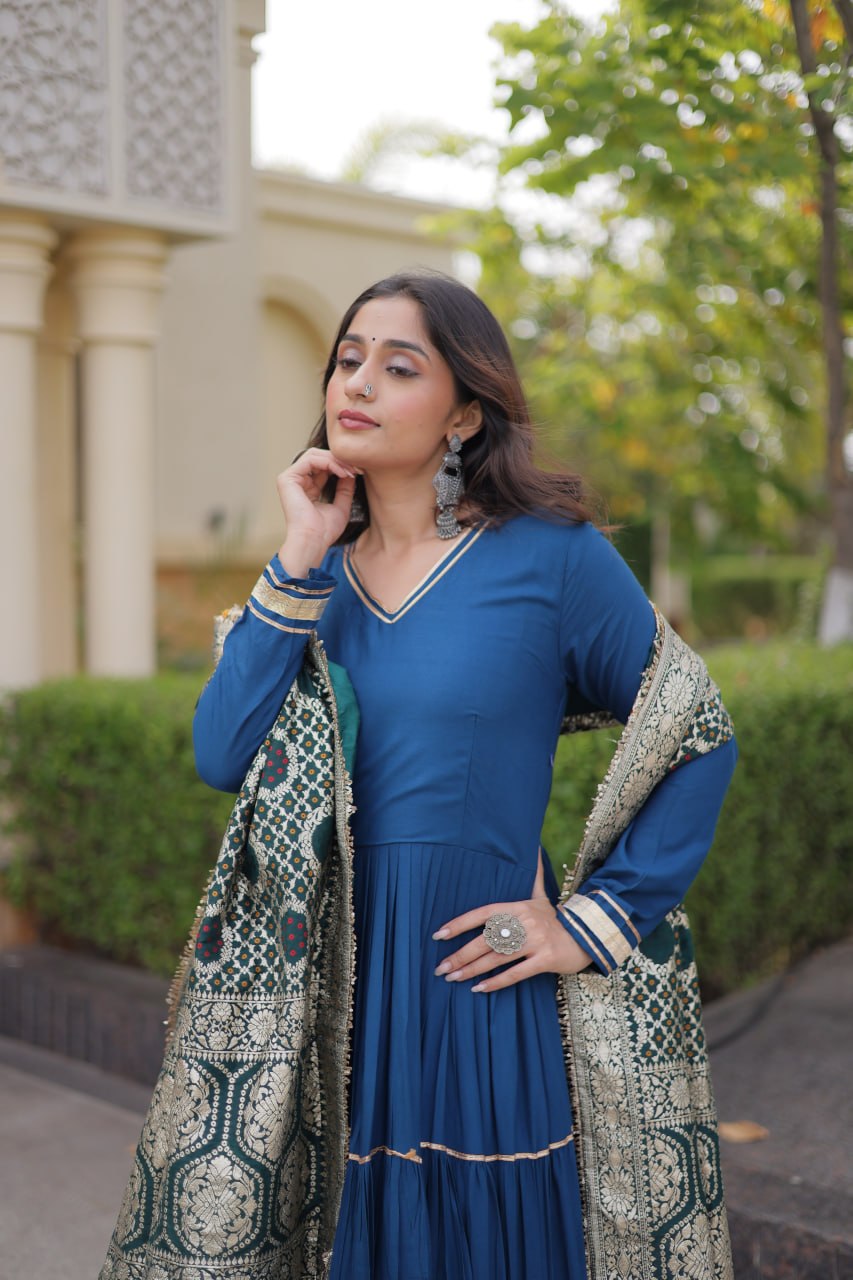 Three-quarter portrait shot of a model in a peacock blue full-sleeve anarkali gown paired with traditional silver jhumkas and statement ring.