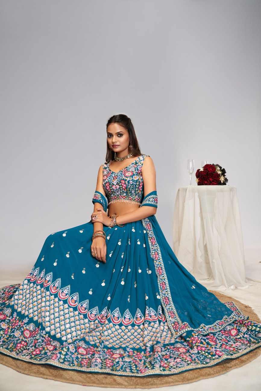 Model seated displaying wide flare of peacock blue lehenga skirt with geometric and floral hem embroidery