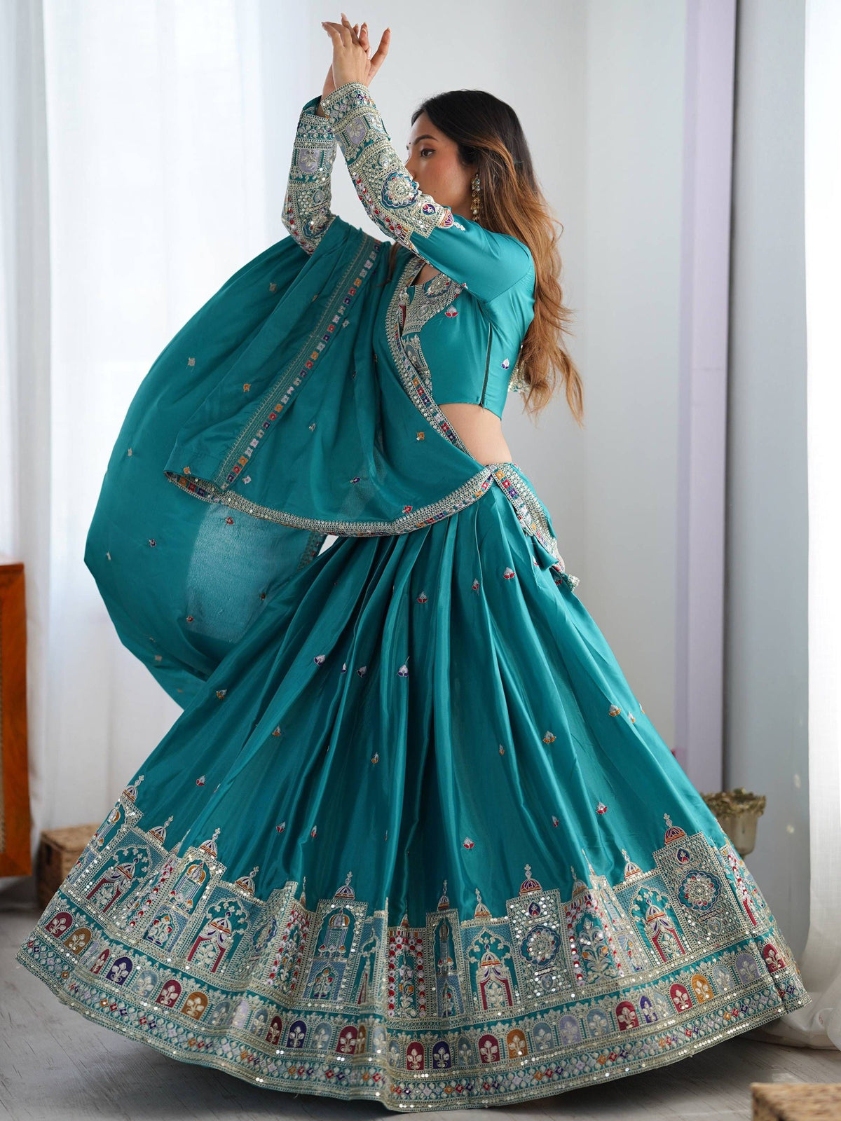 Model in motion showcasing flare of peacock blue pleated lehenga choli with ornate border embroidery