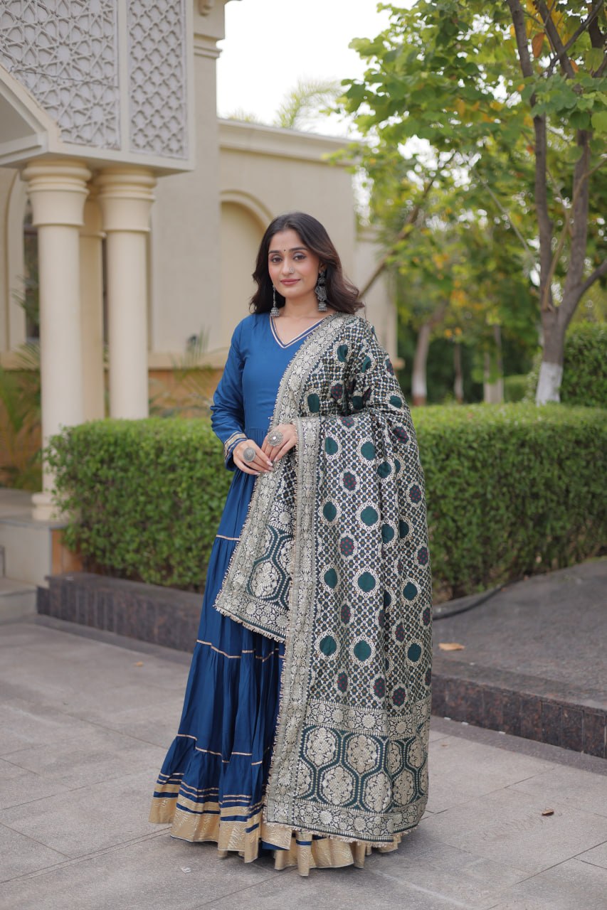Full-length front view of a model wearing a peacock blue tiered anarkali gown paired with an intricately woven green Bandhani dupatta drape.