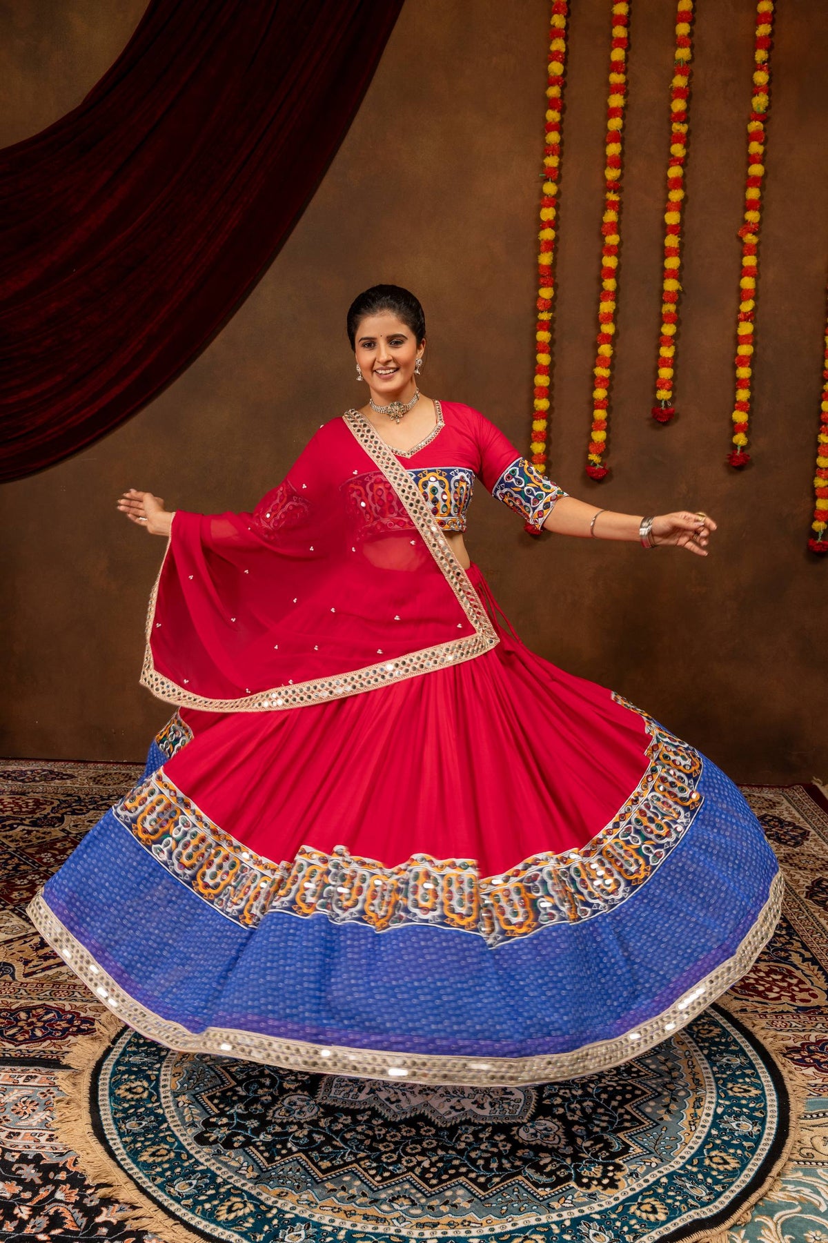 Full flared view of model wearing pink lehenga skirt with blue bandhani print and mirror work border