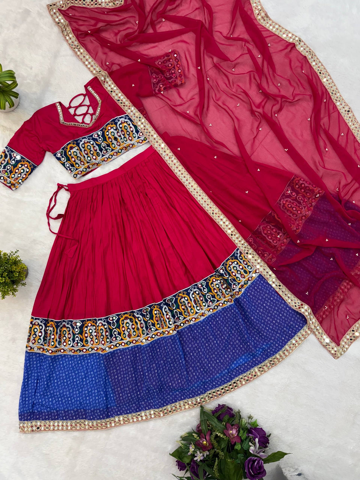 Flat lay view of pink and blue lehenga choli set with dupatta featuring mirror work borders and printed hem