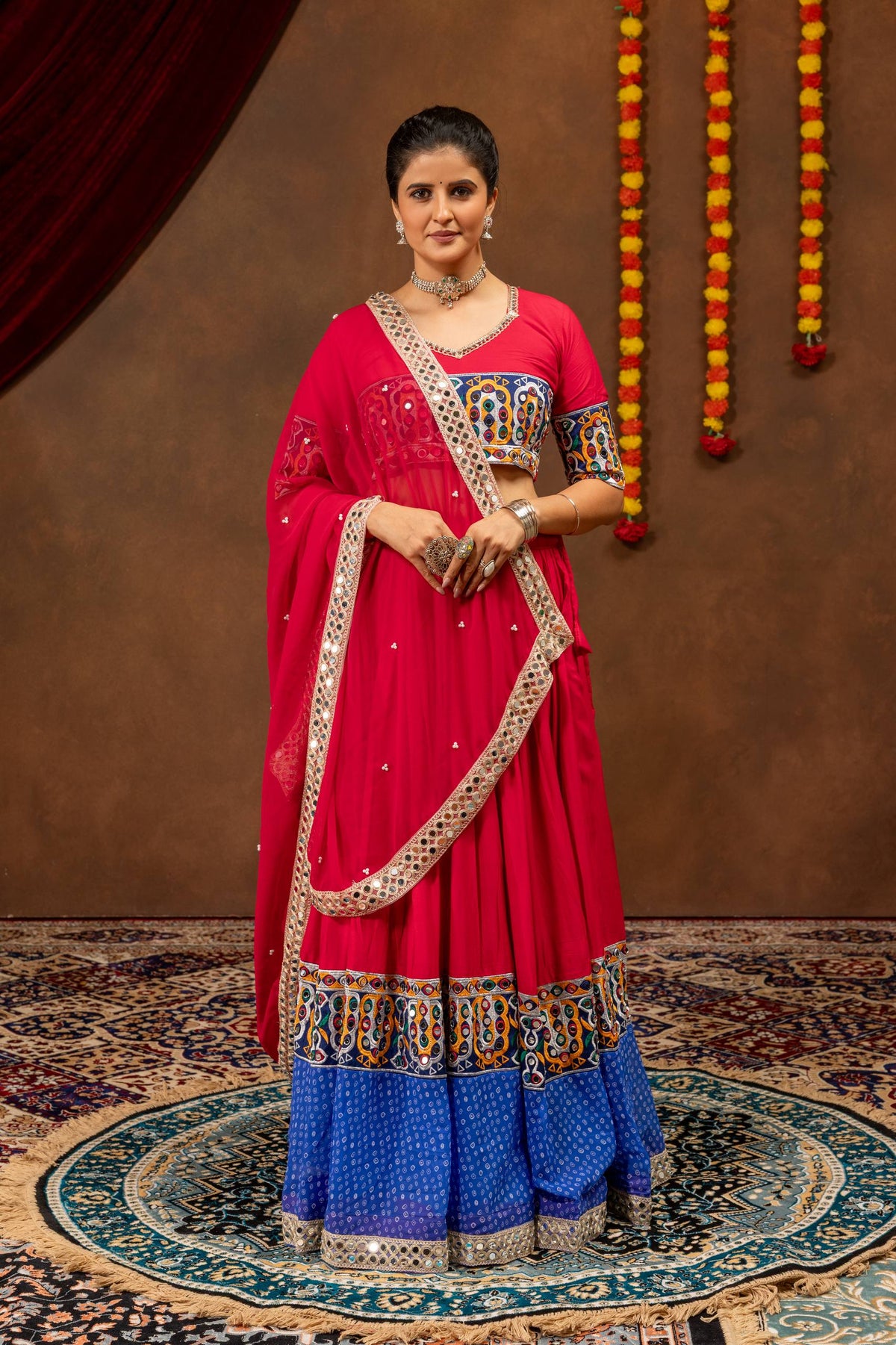 Front view of model standing in pink and blue lehenga choli set with pleats and mirror work detailing