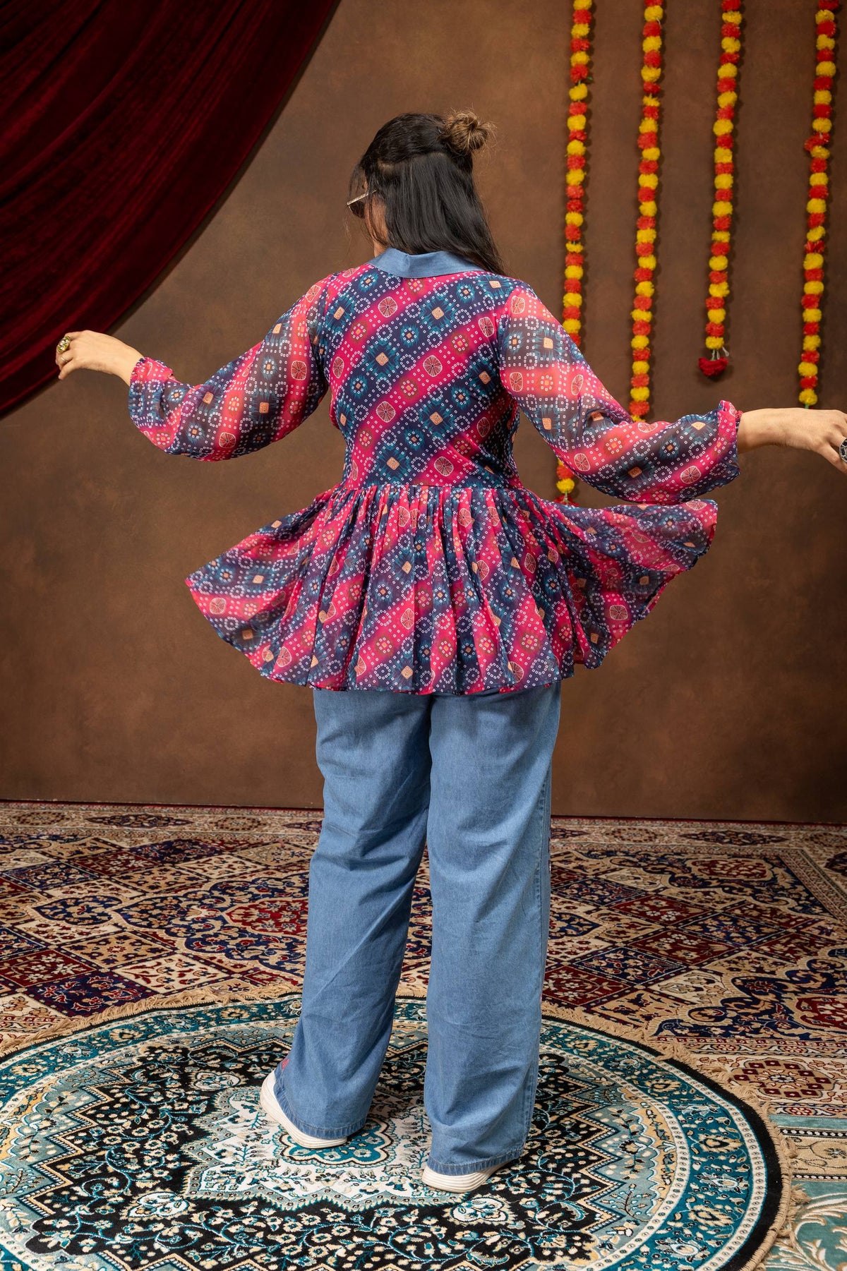Back view of model wearing gathered pink and navy bandhani printed tunic top with wide-leg light blue denim pants