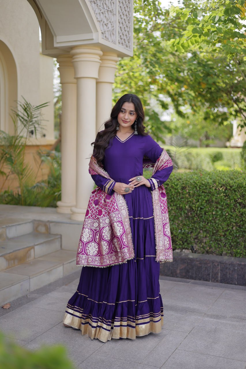 Standing full-length shot of a model in a deep purple flared gown with gold border tiers and contrasting pink woven Banarasi dupatta.