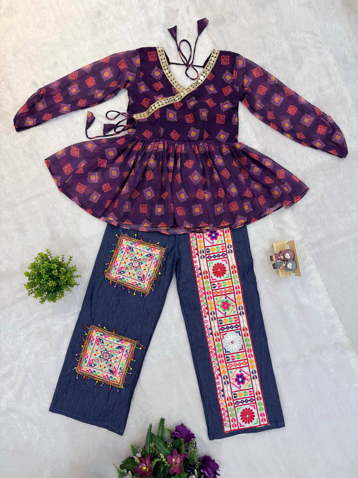 Flat lay view of purple printed angrakha peplum top with mirror lace and blue denim pants featuring embroidered patches