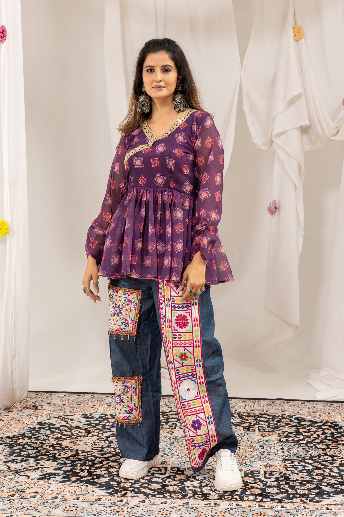 Full-length front view of model wearing purple printed overlap angrakha tunic and wide embroidered denim trousers