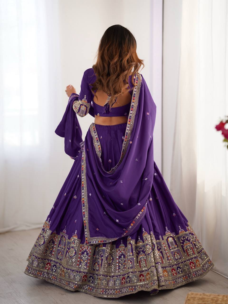 Back view of model wearing purple pleated lehenga choli with tie-up back blouse and heavy border skirt