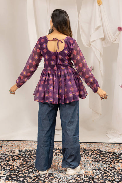 Back view of model wearing purple printed peplum top with tie-up back neckline and wide-leg denim jeans