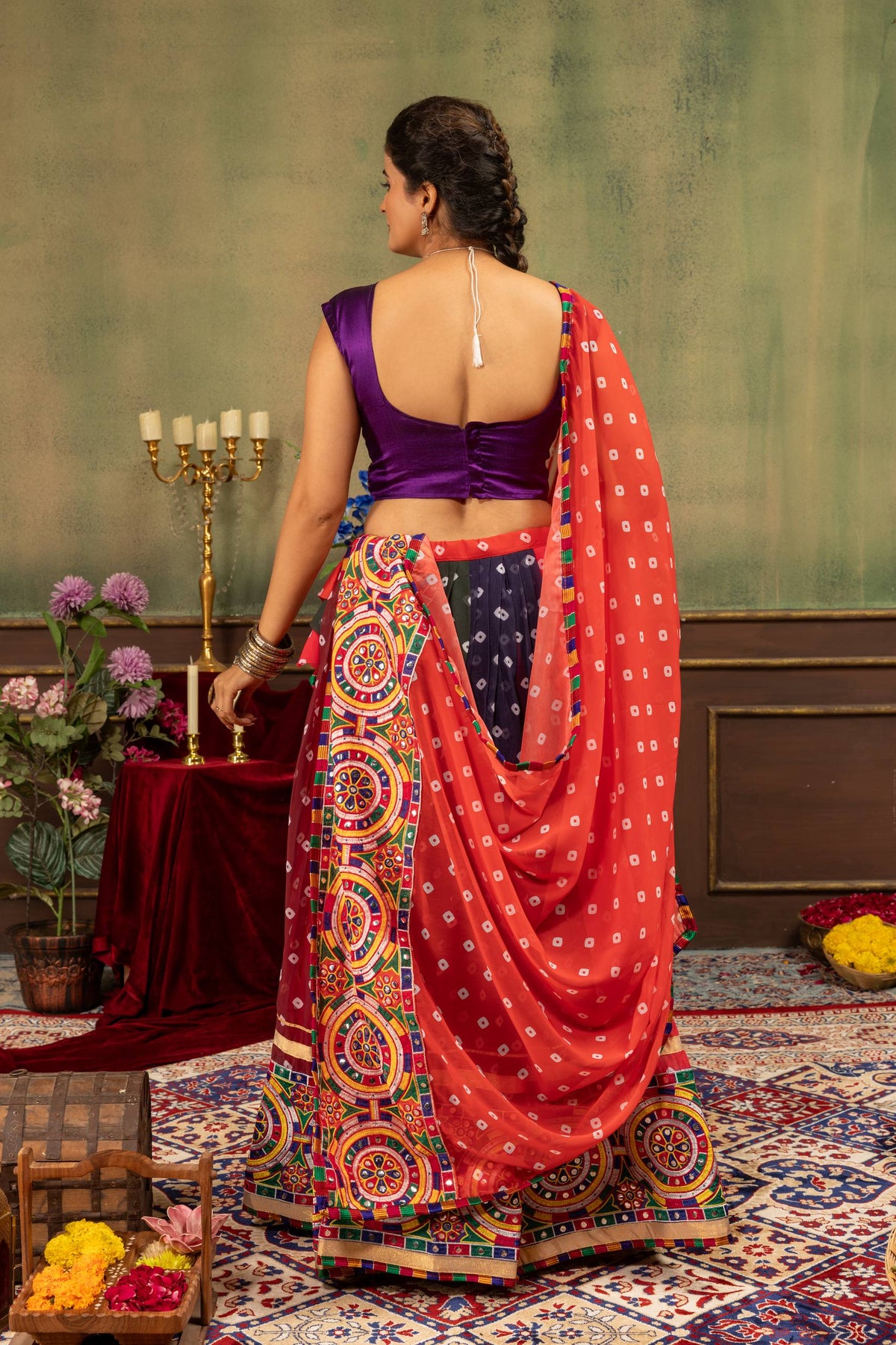 Back view of model wearing purple sleeveless blouse and flared bandhani skirt with draped red dupatta
