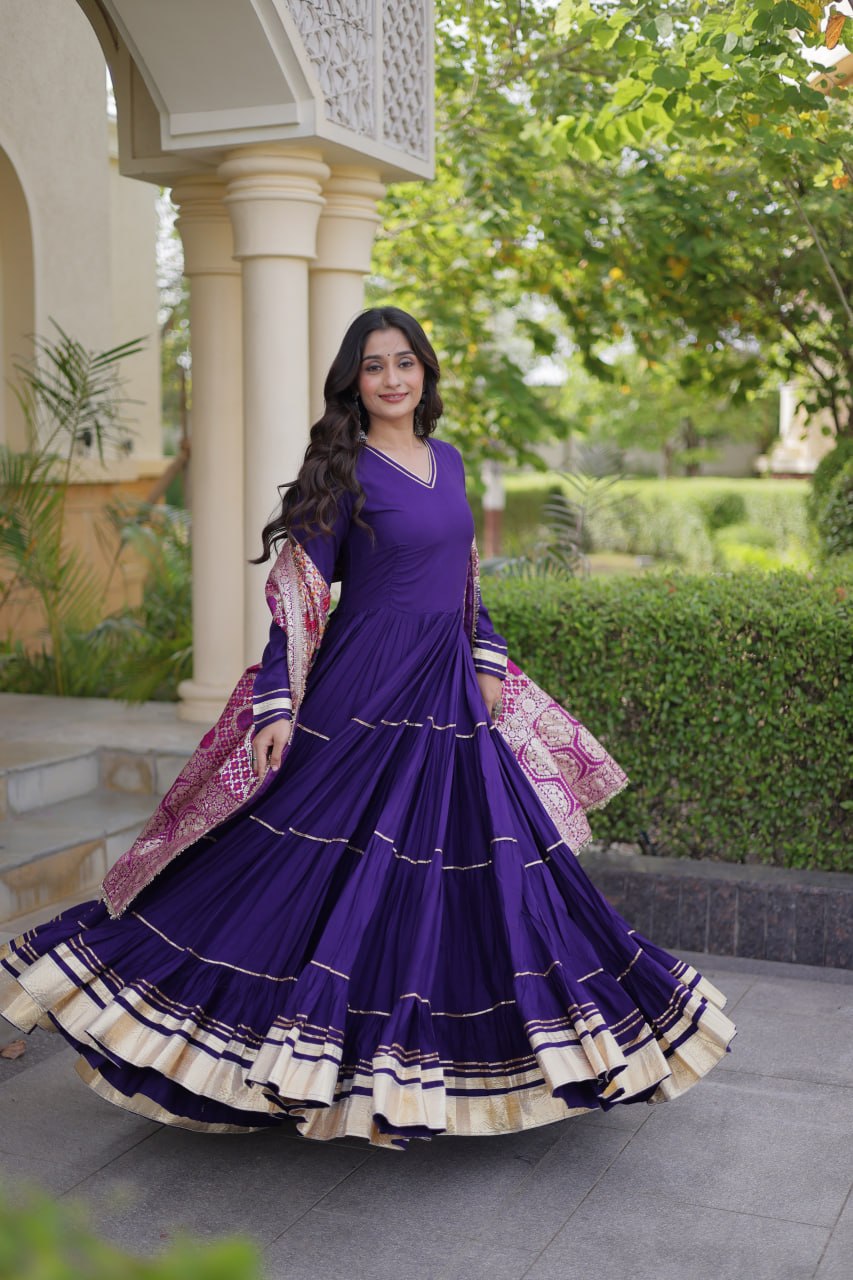 Dynamic full-length shot capturing the wide gathered flare and gold border hemline of a royal purple tiered anarkali dress.