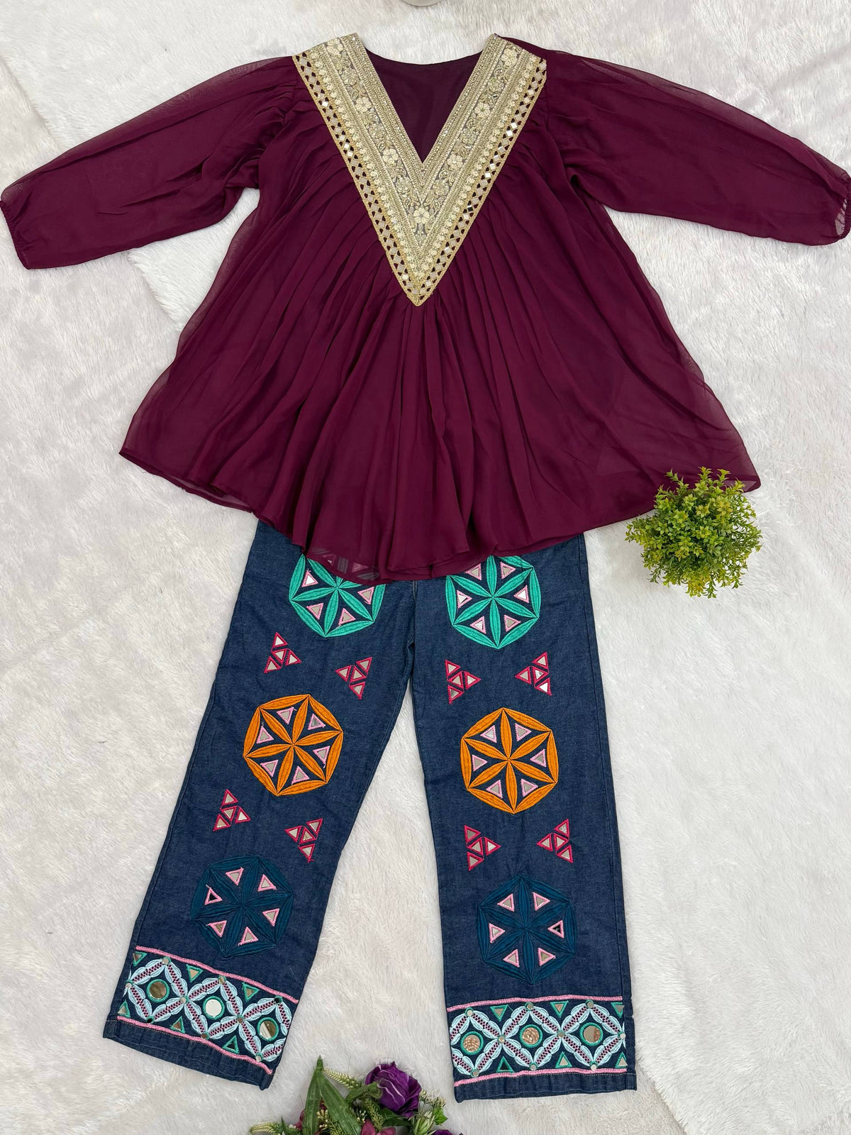 Flat-lay display of purple v-neck tunic top and blue jeans with colorful geometric embroidery and mirror work