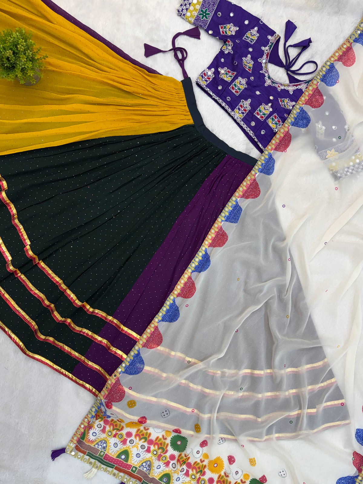 Flat lay view of purple, dark green, and yellow panelled lehenga skirt, embroidered purple blouse, and white scallop-border dupatta
