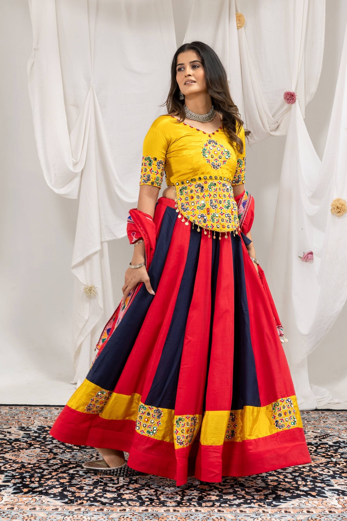 Model in side-angle pose wearing red and navy blue kalidar lehenga skirt with yellow embroidered border and blouse