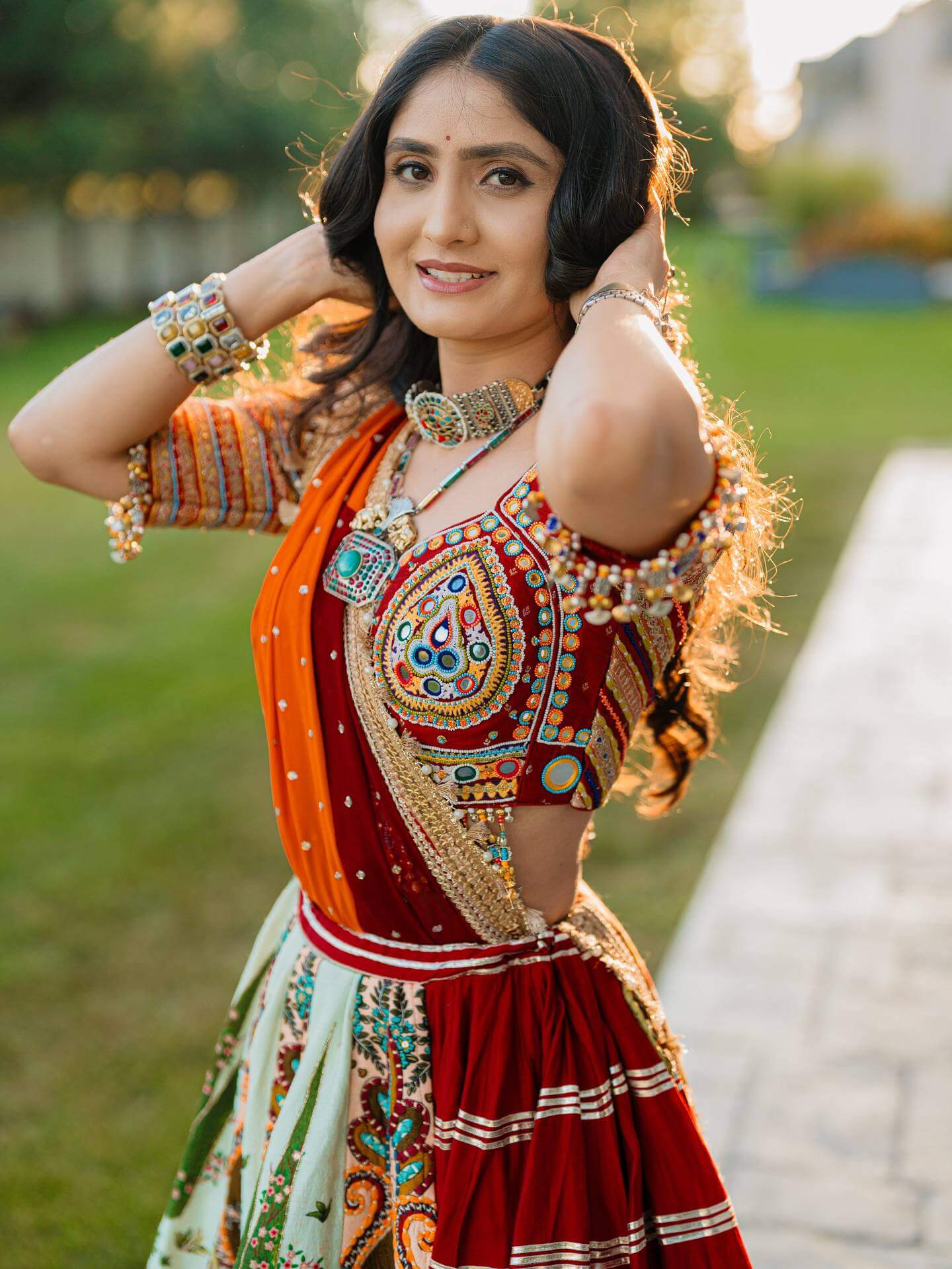 Mid-shot view of model wearing a red square-neck blouse with colorful teardrop mirror embroidery and draped orange dupatta