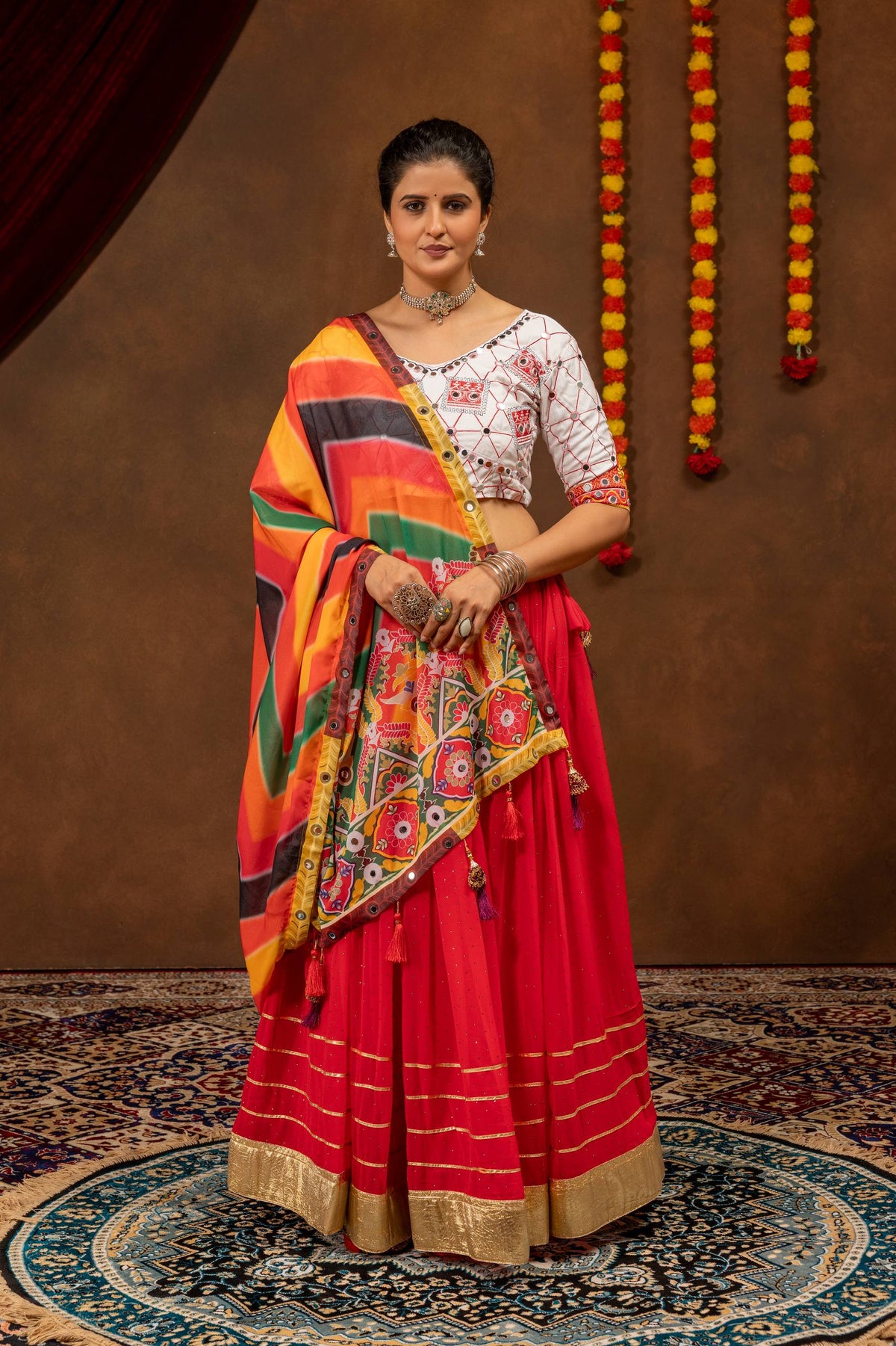 Model in a full-length pose wearing a red flared lehenga with a white embroidered blouse and draped multicolor printed dupatta.