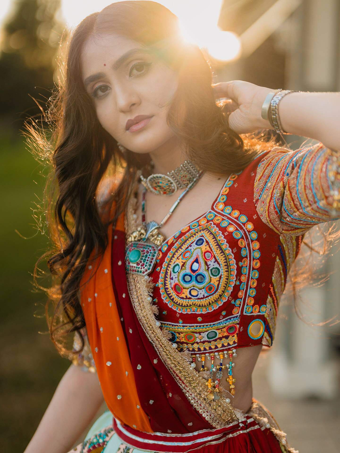 Close-up of red choli blouse highlighting dense threadwork, center mirror motif, and multicolor beaded hanging fringe