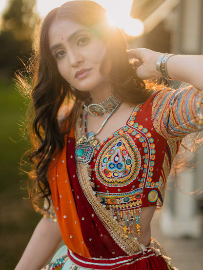 Close-up of red choli blouse highlighting dense threadwork, center mirror motif, and multicolor beaded hanging fringe